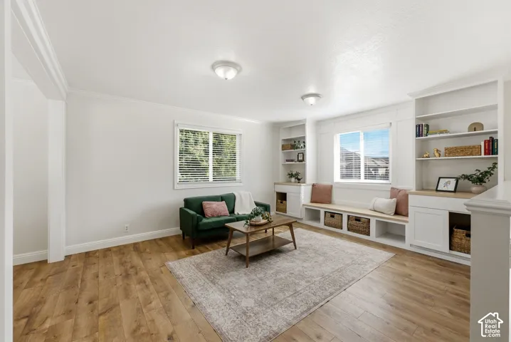 Wood-finish flooring, built-in shelving, white cabinetry, integrated window bench, and crown molding