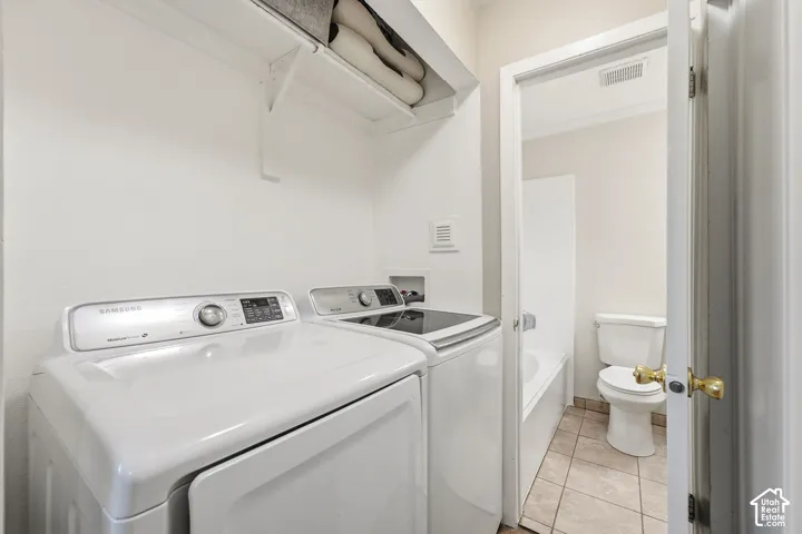 Laundry area with built-in shelving, tile flooring, and direct access to a full bathroom featuring a white bathtub and toilet