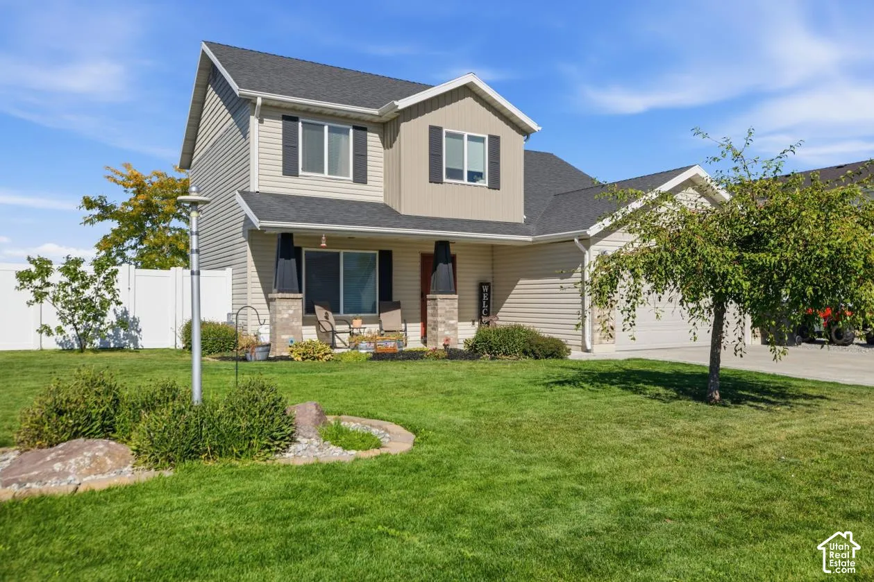 Two-story exterior with a covered front porch featuring stone-clad columns, an attached garage, and a white privacy fence