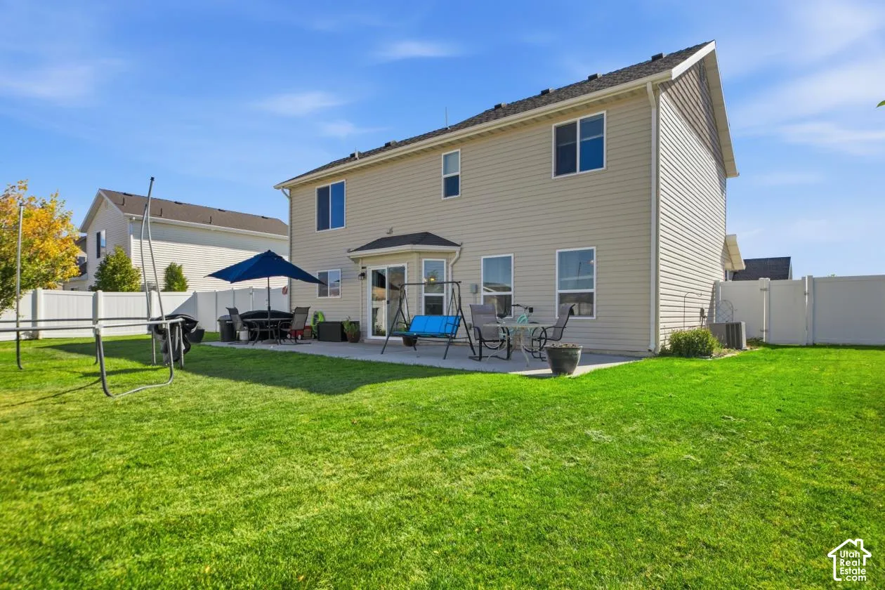 Expansive backyard featuring a large green lawn, concrete patio, and a privacy fence