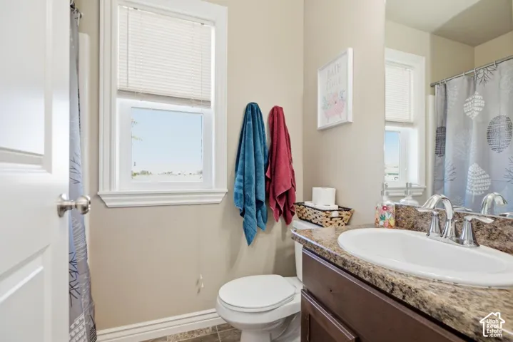 Bathroom featuring a single window, a toilet, an integrated sink with a chrome faucet, and a vanity with a stone-finish countertop