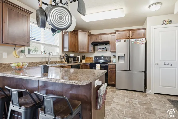 Kitchen with wood cabinetry, stone-look countertops, stainless steel refrigerator, black range, and durable tile flooring