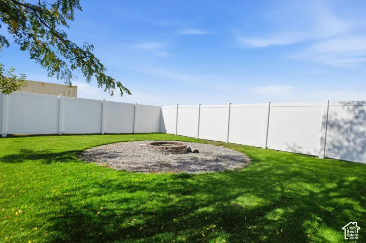Expansive yard featuring a manicured lawn, full perimeter white privacy fencing, and a built-in stone fire pit with gravel surround