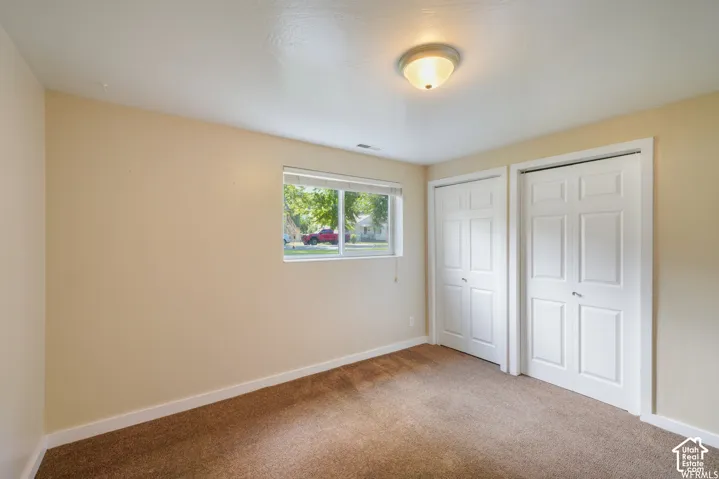 Neutral wall color, two panel-style closet doors, single window, flush mount ceiling light fixture, and carpet flooring