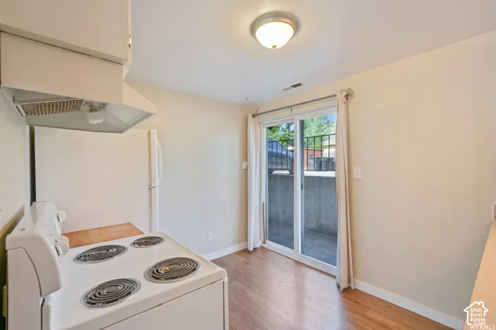 Full-size white refrigerator, white electric range with overhead exhaust hood, sliding glass door, hard-surface flooring, and neutral wall paint