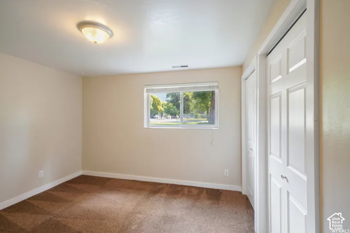 Neutral wall paint, brown carpeting, white trim, a single window with blinds, and white bi-fold closet doors