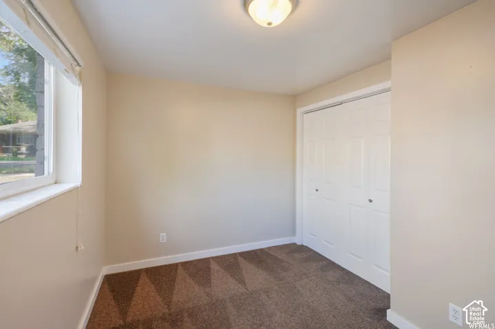 Neutral wall color, patterned carpet, window with white trim, and bi-fold closet doors