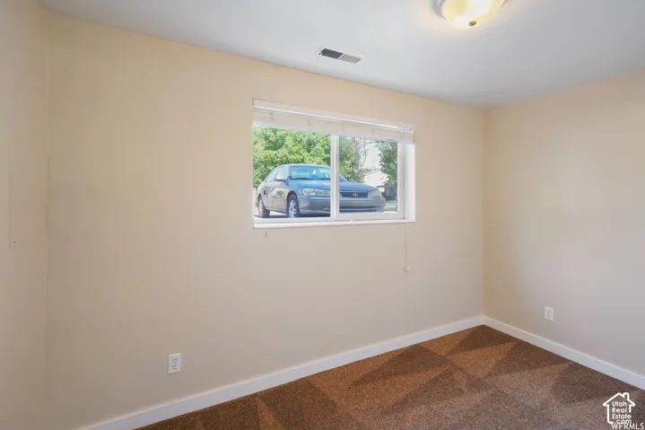 Recessed window with blinds, light-toned wall paint, white trim, patterned carpet flooring, and an overhead flush-mount light fixture