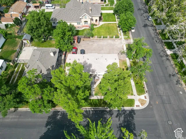 Residential property featuring a gray shingle roof, mature landscaping, and an asphalt parking area