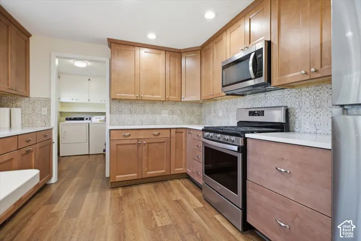 Wood-finish flooring, light wood cabinetry, stone tile backsplash, stainless steel range, and stainless steel microwave