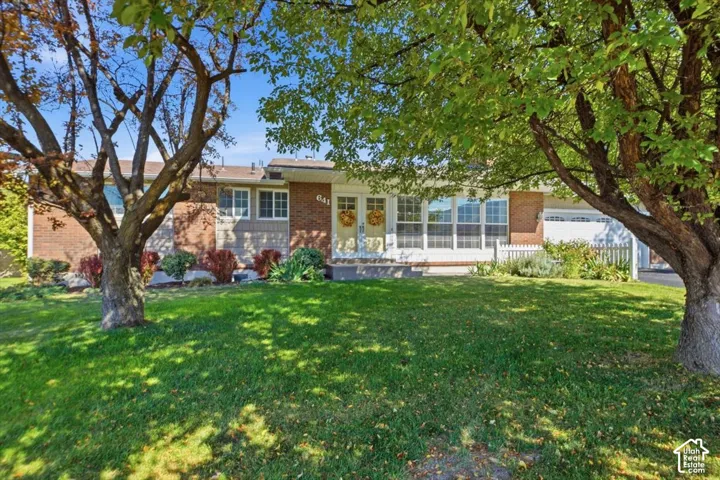 Brick and siding exterior with a large front lawn, mature trees, and a white picket fence