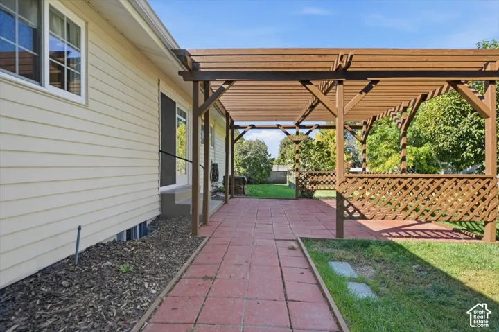 Expansive patio featuring a wooden pergola and lattice railing, red paver flooring, and direct access to the exterior