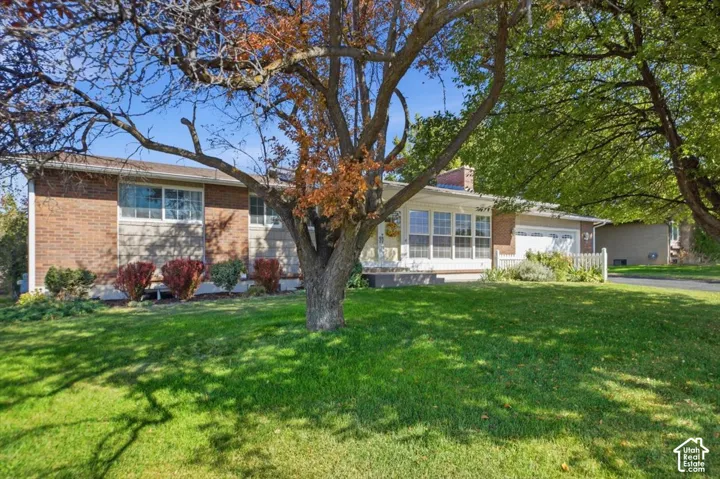 Brick and siding exterior with a prominent front lawn, mature trees, and an attached garage