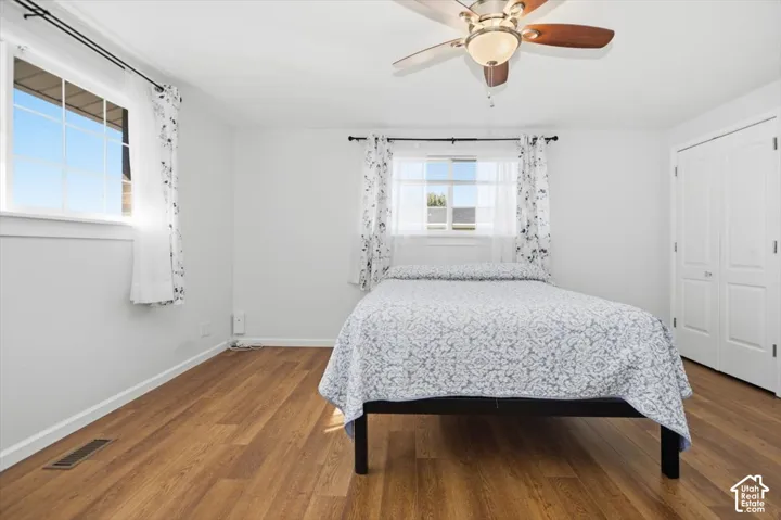 Bright room featuring wood-finish flooring, white walls, two windows, a ceiling fan, and double bi-fold closet doors