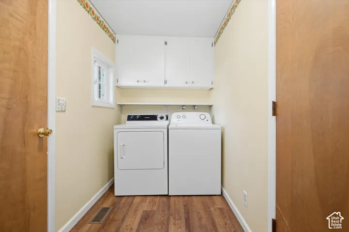 Utility area featuring wood-finish flooring, white cabinetry, and a window for natural light