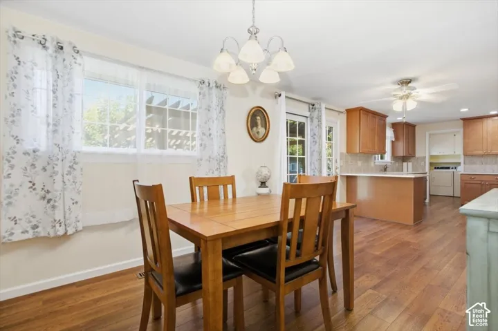Dining room and kitchen featuring wood-finish flooring throughout, a wooden dining table with seating for four, wood cabinetry with stainless steel appliances, pendant lighting, and expansive windows with natural light