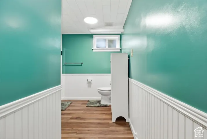 Bathroom with wood-finish flooring, white wainscoting, and a compact window