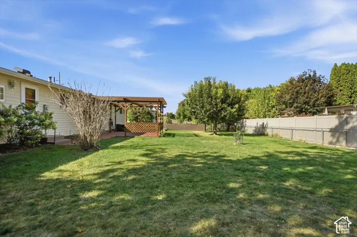 Spacious backyard featuring a covered patio, expansive lawn, mature trees, and privacy fencing