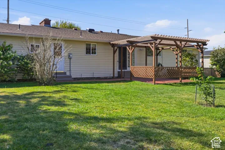 Expansive backyard featuring a pergola-covered deck with lattice detailing, a large grassy area, and mature shrubs