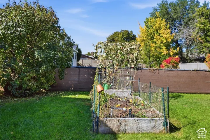 Expansive lawn featuring mature landscaping, raised garden beds, and a privacy fence