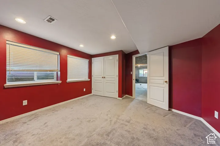 Recessed lighting, two windows with blinds, gray carpet, white bi-fold closet doors, and white trim
