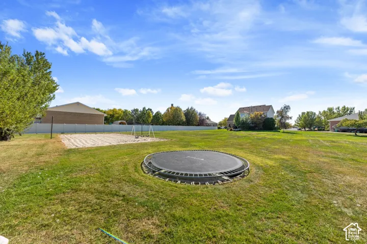 Expansive grass lawn featuring a sand court and perimeter fencing