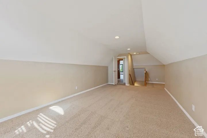 Carpeted room with sloped ceilings, recessed lighting, and a neutral color palette