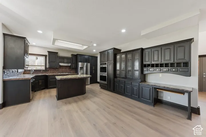 Spacious kitchen featuring dark cabinetry, granite countertops, a central island, stainless steel appliances, and wood-finish flooring