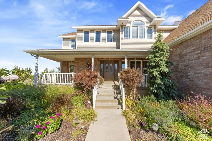 Inviting front entry with a covered porch, brick and siding exterior, concrete walkway, and established landscaping