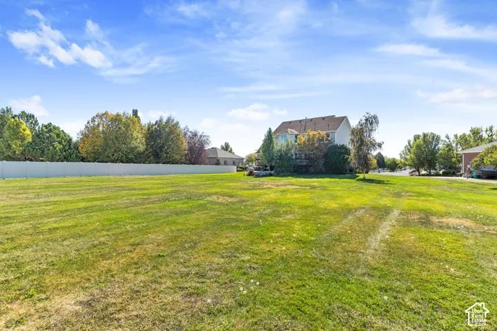 Expansive green space with a residential structure, mature trees, and a privacy fence
