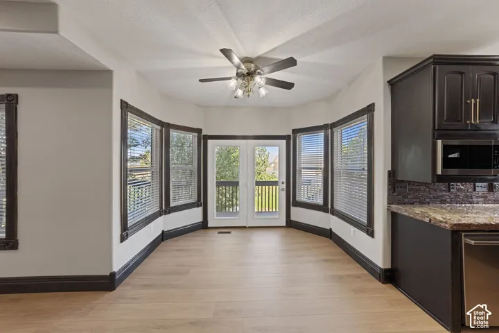 Light wood-finish flooring, dark wood trim, multiple windows with blinds, built-in dark wood cabinetry, and a ceiling fan with integrated lighting