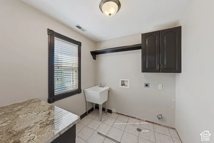 Utility room featuring a utility sink, tiled flooring, dark wood-finish cabinetry, a window with blinds, and a built-in shelf