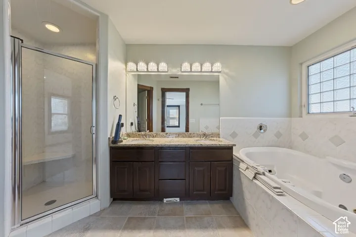 Dual vanity with granite countertop, built-in soaking tub, separate glass-enclosed shower, tiled flooring, and accent tile work