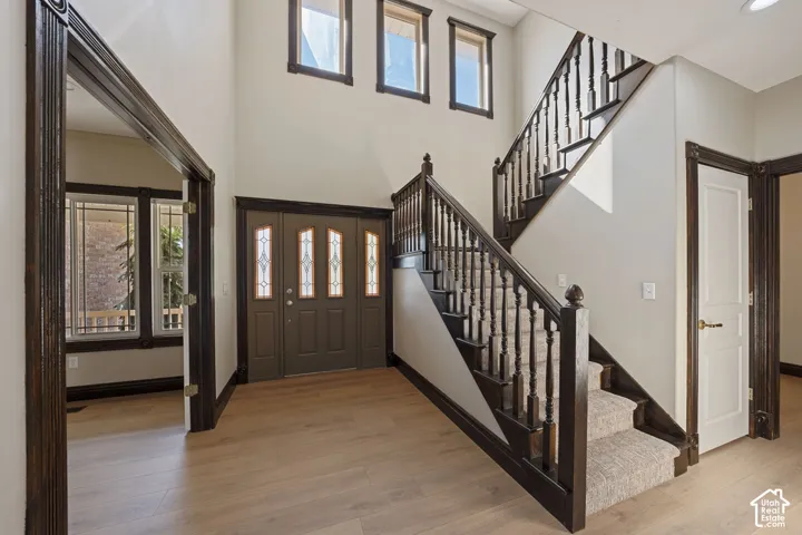 Two-story foyer featuring wood-finish flooring, a grand staircase with dark wood newel posts, and a double entry door with decorative glass inserts
