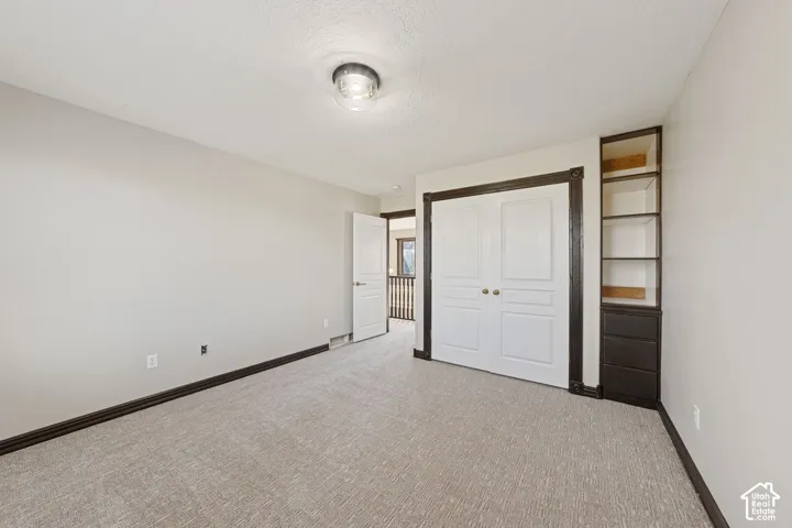 Built-in shelving with drawers, recessed closet with bi-fold doors, white interior door with dark trim, ceiling-mounted light fixture, light-colored carpeting