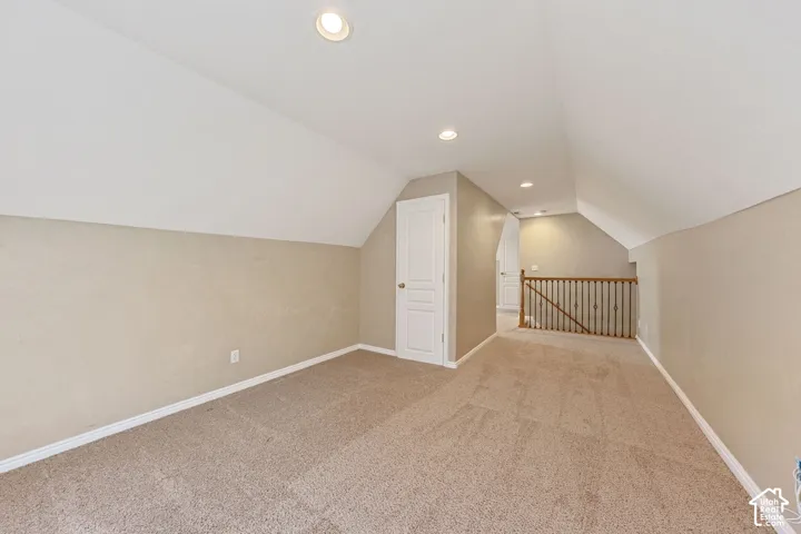 Recessed ceiling lighting, sloped ceiling design, neutral carpet flooring, warm-toned wall finishes, and white interior doors