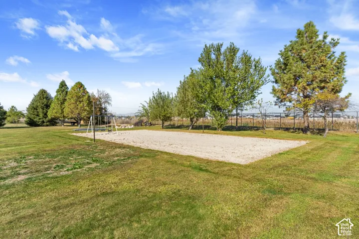 Expansive lawn area with a sand court, established trees, and perimeter fencing