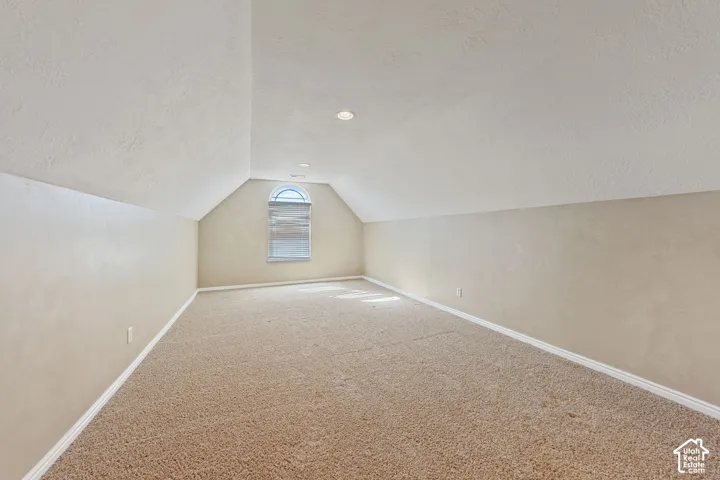 Carpeted room with sloped ceilings, recessed lighting, and an arched window