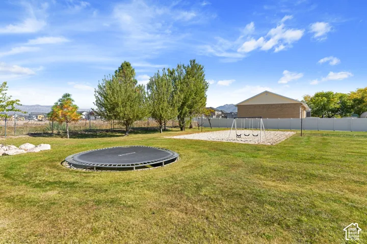 Expansive grass lawn with an in-ground trampoline and a dedicated sand play area featuring a swing set