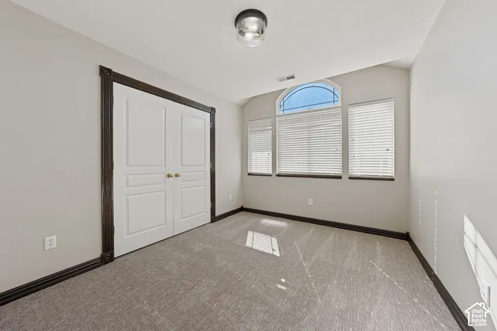 Textured carpet flooring, white painted walls, white double doors with gold-toned hardware, dark wood-finish trim, and a window arrangement featuring an arched transom and horizontal blinds