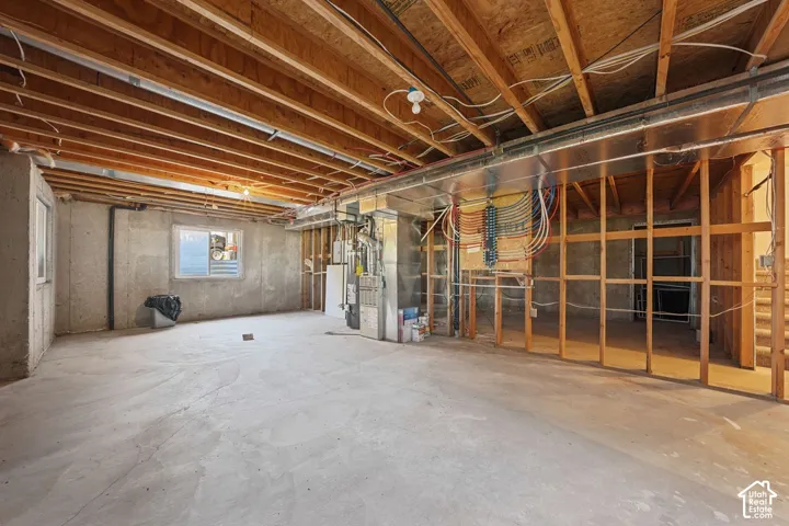 Unfinished basement with exposed ceiling joists, concrete floor, framed interior walls, and visible utility connections