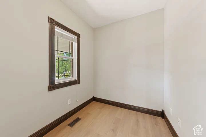 Light wood-finish flooring, dark-stained decorative window trim, white walls, and dark-stained baseboards