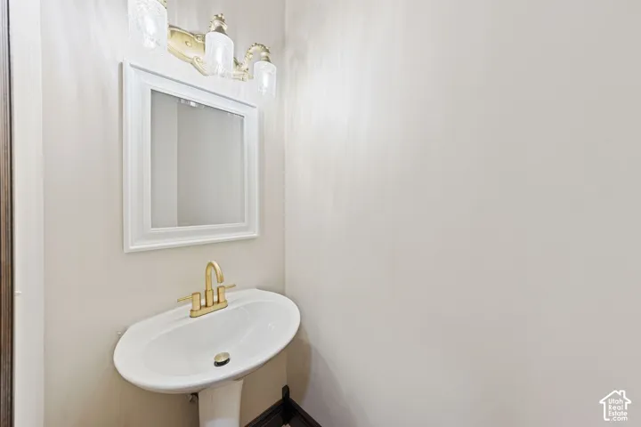 Pedestal sink with brass-finish faucet, framed mirror, and decorative wall-mounted light fixture
