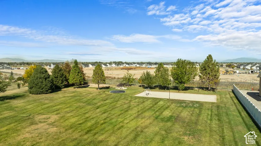 Expansive backyard featuring a manicured lawn, established trees, and a sand court