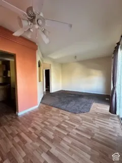 Vaulted ceiling with a ceiling fan, wood-finish flooring, and a carpeted area