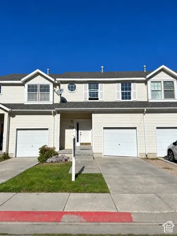 Light-colored siding exterior with dormer windows, an octagonal window, and white garage doors