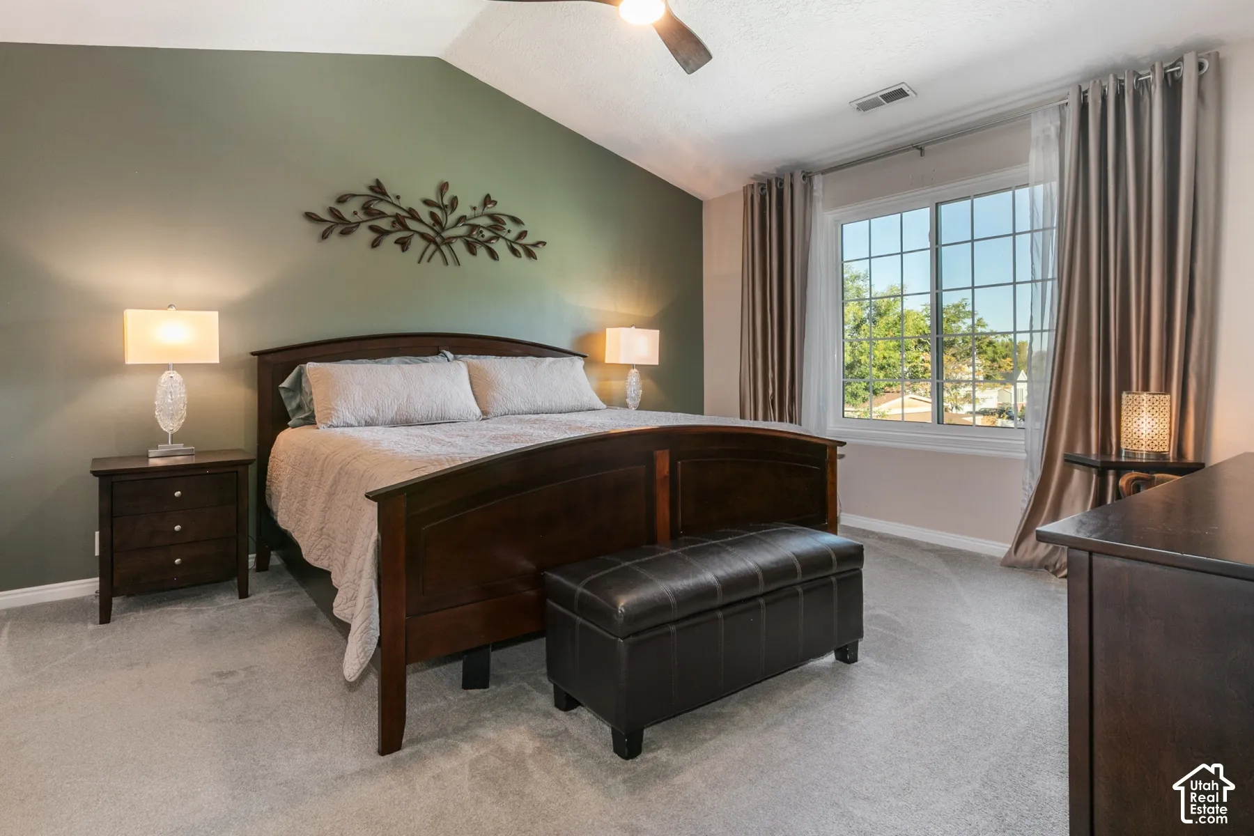 Vaulted ceiling, ceiling fan, large grid window, soft gray carpeting, and accent wall