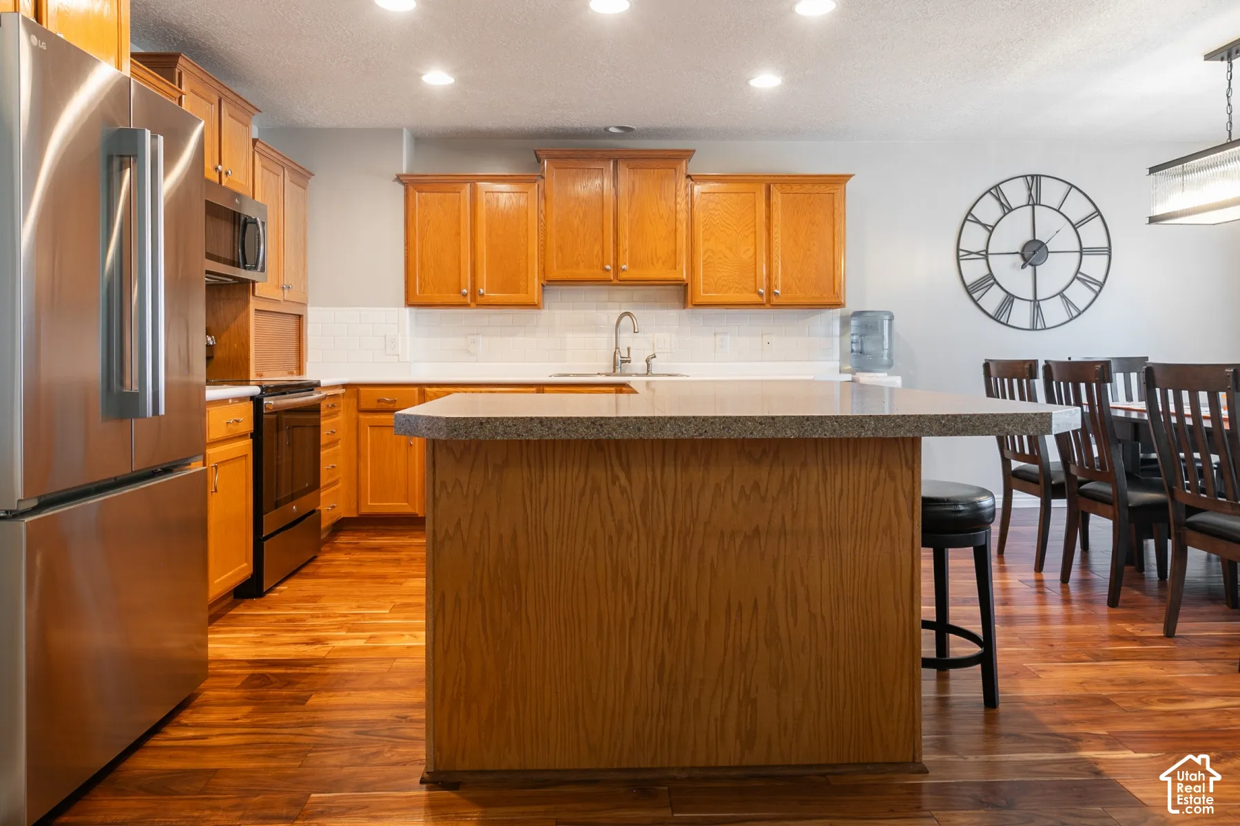 Kitchen featuring stainless steel appliances, wood-finish flooring, wood cabinetry, light-toned countertops, and a white subway tile backsplash