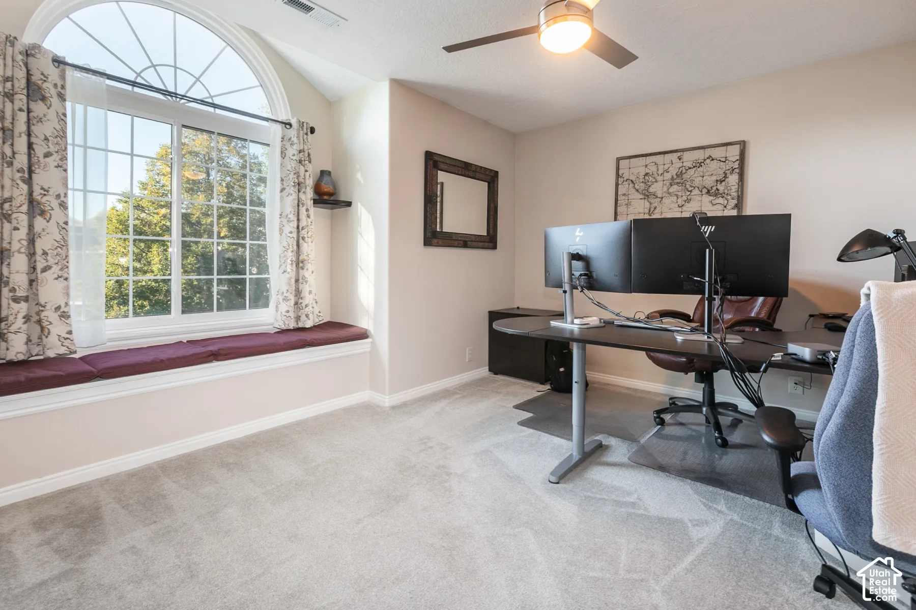 Arched window with gridded panes, window seating with cushion, ceiling fan with integrated lighting, and neutral-toned carpeting