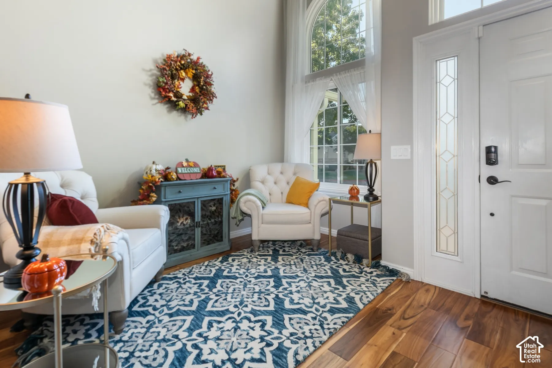 Hardwood flooring, arched window with white trim, white entry door with decorative glass insert, light gray wall paint